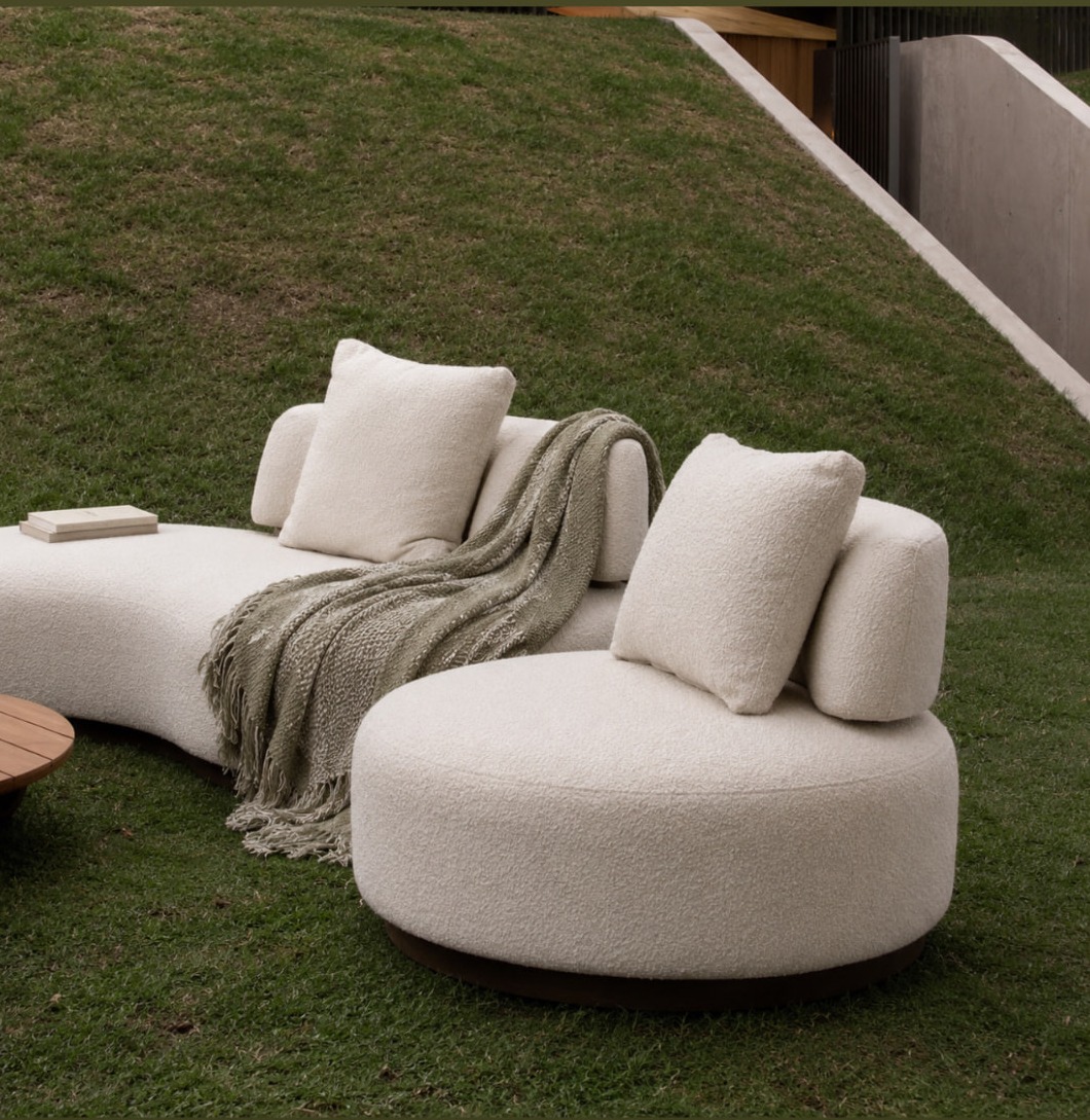Sofá curvo e poltrona redonda em bouclé off-white sobre gramado de jardim