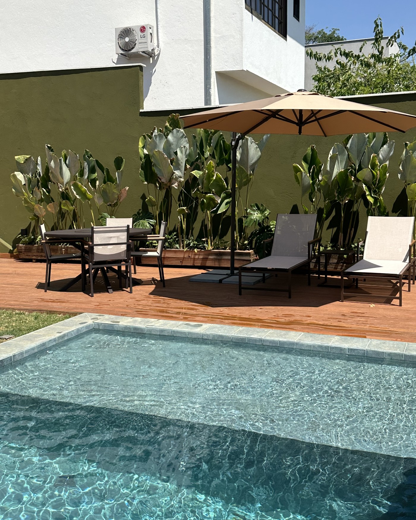 Deck de piscina com mesa de refeições, cadeiras, espreguiçadeiras e ombrelone
