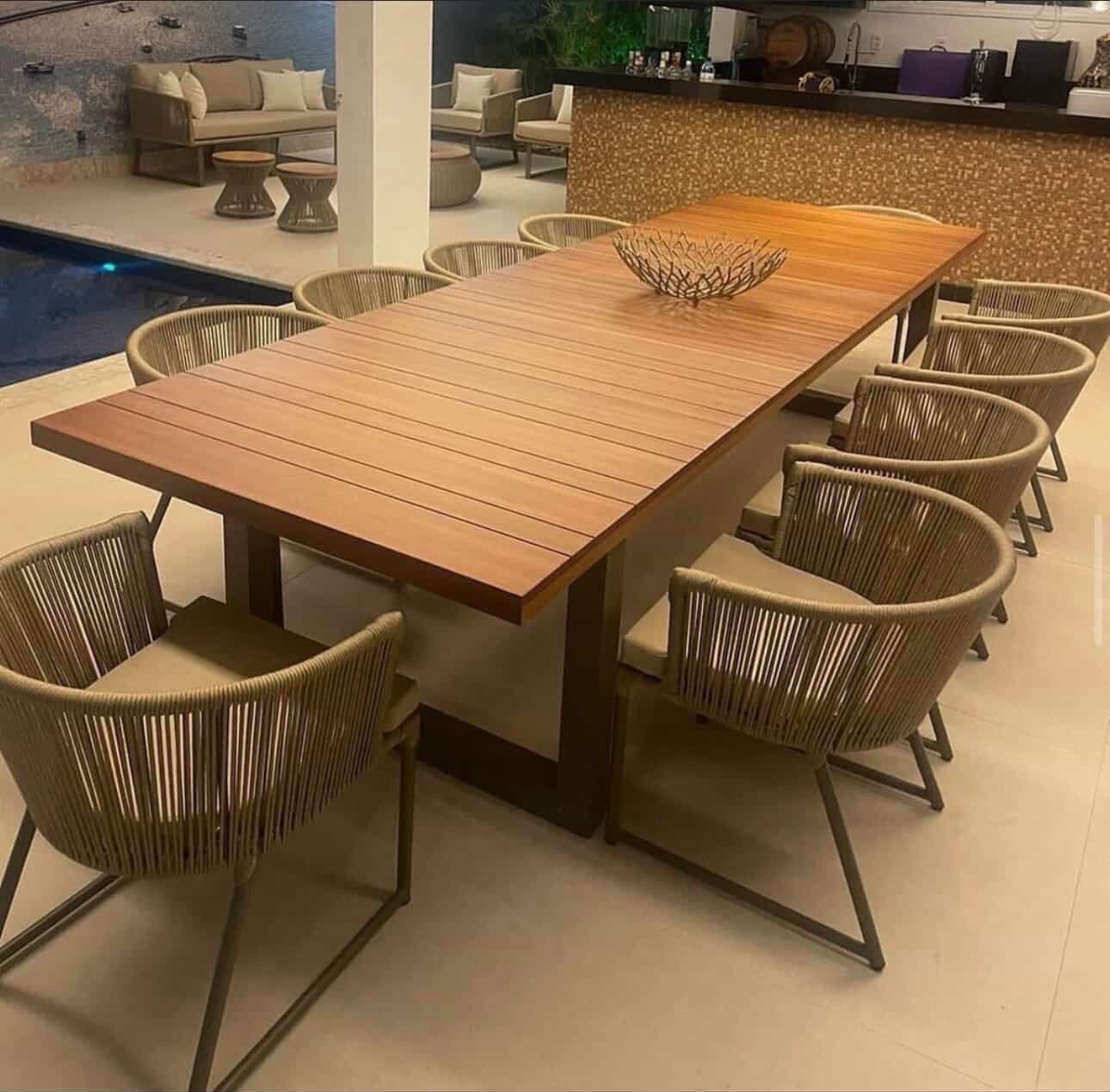 Mesa longa de jantar em madeira com cadeiras de corda à beira da piscina