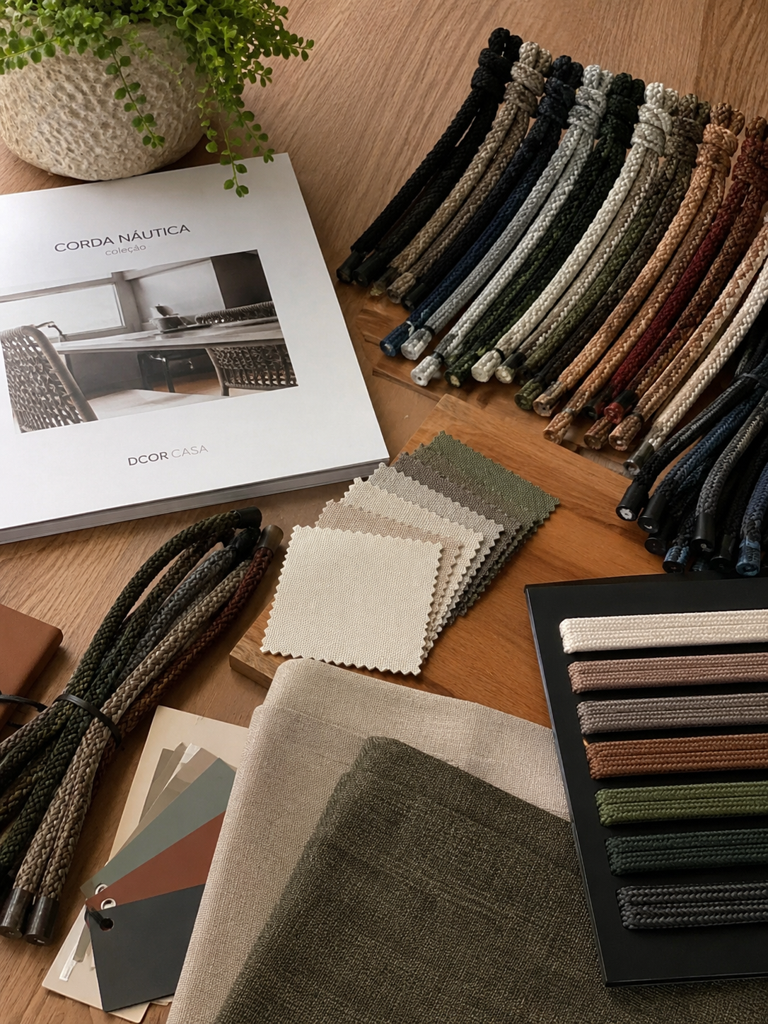 Catálogo Dcor Casa com amostras de corda náutica, tecidos e cartela de cores sobre mesa de madeira